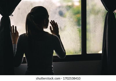 Young Lonely Woman Looking Out Through The Window of Her House During The Coronavirus Pandemic Quarantine Lockdown. Stay at Home