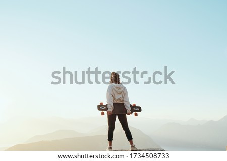 
Young long boarder woman with dreadlocks  standing on top of mountain in beautiful scenic nature in Montenegro at sunset. Freedom concept
