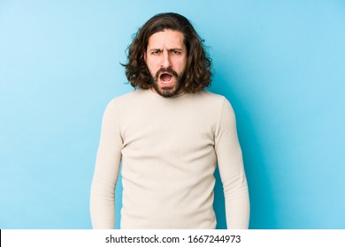 Young Long Hair Man Isolated On A Blue Background Screaming Very Angry And Aggressive.