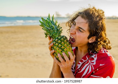 Young Long Hair Man In Red Hawaiian Shirt Opening Mouth To Bite Pineapple Fruit At The Beach