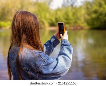 Young Long Haired Red Head Female In A Denim Jacket Operating A Smart Phone With Orange Case Outside