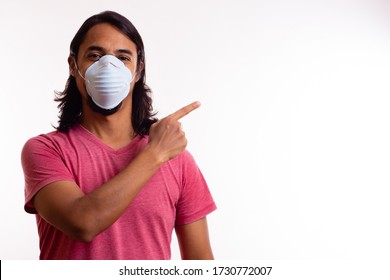 Young Long-haired Latino Man With Face Mask Pointing His Hand To The Right Above. Coronavirus Concept.