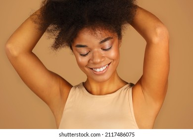 Young lovely african american model with closed eyes and arms raised demonstrating smooth clean armpits without hair, posing isolated over beige studio wall background. Depilation and epilation