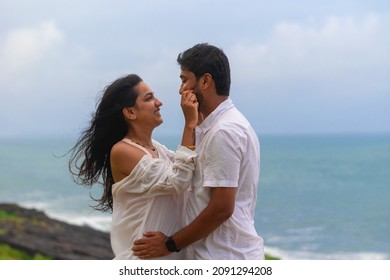 A young lovely attractive couple looking at each other, embracing, making love, smiling, cuddling at beach on vacation, holiday, honeymoon, trip to India, Maldives, Asia, foreign beach, cliff, sunset.