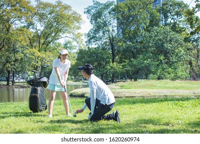 Young lovely couple playing golf together on a course near a lake, boyfriend teaching his girlfriend how to play golf. happy time in summer, concept of union and love