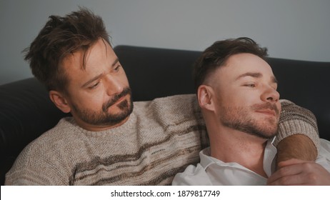 Young Lovely Gay Couple Cuddling And Relaxing On The Couch. Different Family Lifestyle Concept Love And Care. High Quality Photo