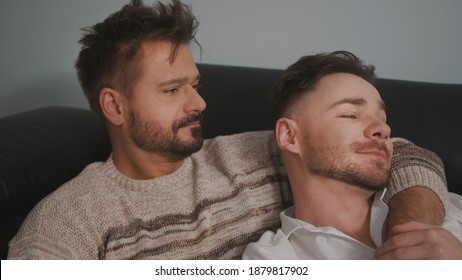 Young Lovely Gay Couple Cuddling And Relaxing On The Couch. Different Family Lifestyle Concept Love And Care. High Quality Photo