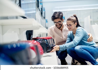 Young Lovely Husband And Wife Deciding Which Vacuum Cleaner To Buy In The Electronic Store.