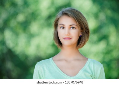 Junge schöne lächelnde Frau in einer grünen Bluse mit kurzen Haaren, Nahaufnahme im Sommerpark.