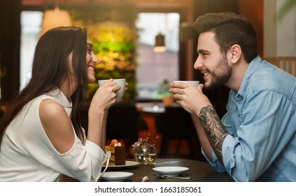 Young Lovers Enjoying Coffee Drinks Together During Romantic Date In Cafe. Love And Dating. Side View
