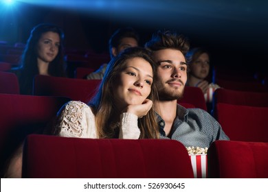 Young loving couple at the cinema watching a movie, he is hugging her girlfriend