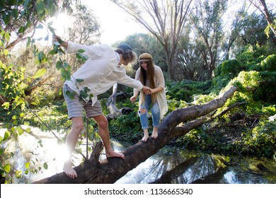 Young loving couple crossing a stream on a fallen log in Secret Garden, Gwelup, Careniup, Western Australia.
