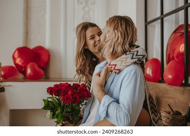 Young loving couple embracing and holding red roses bouquet while celebrating Valentines day at home - Powered by Shutterstock