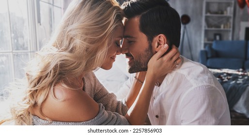Young loving couple embracing and touching noses while sitting face to face indoor - Shutterstock ID 2257856903