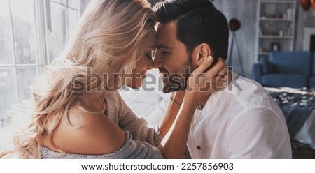 Young loving couple embracing and touching noses while sitting face to face indoor
