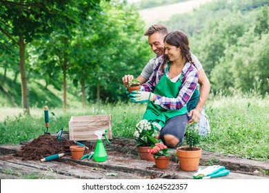 Young loving couple have fun with gardening work on a wooden floor during spring day - Millennial are dressed with green aprons - Powered by Shutterstock