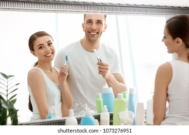 Young Loving Couple Looking In Mirror While Brushing Teeth Indoors