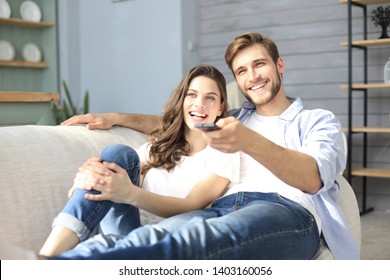 Young loving couple on sofa at home watching tv and laughing.