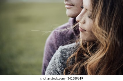 Young loving couple outdoors sitting on grass, hugging and looking away, future and relationships concept - Shutterstock ID 341389619