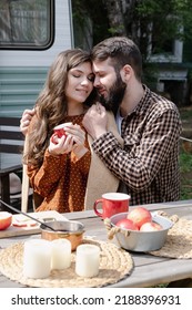 Young Loving Couple Is Traveling In Travel Van. Romantic Atmosphere Of Relaxation. Road Trip Around Country For The Weekend. Male And Female Embrace Near Camper And Drinking Tea Or Mulled Wine