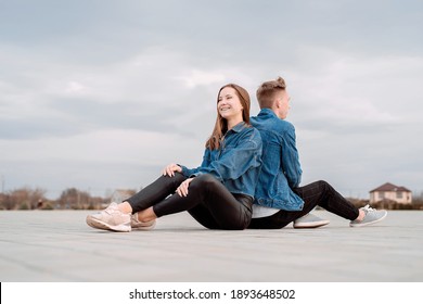 Young Loving Couple Wearing Jeans Sitting Back To Back In The Street Spending Time Together