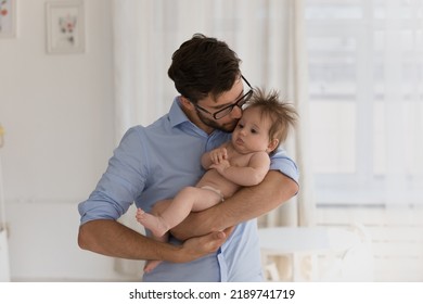 Young loving daddy standing in cozy warm domestic room hugs and kisses gently with love his cute newborn, lulls before daytime nap looking happy being father. Protection, adoption, family bond - Shutterstock ID 2189741719