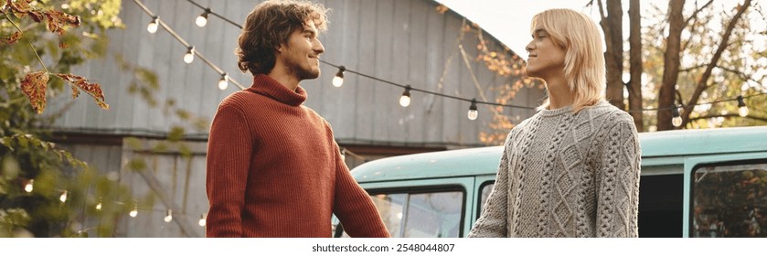 Young loving gay couple dressed in warm sweaters share a moment in an autumn landscape. The soft glow of string lights illuminates their surroundings, creating a cozy atmosphere near a vintage van. - Powered by Shutterstock