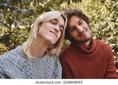 Young loving gay couple enjoy each others company in a lush garden filled with greenery. They wear cozy sweaters and share warm smiles, capturing a moment of friendship and affection under the sun. - Powered by Shutterstock