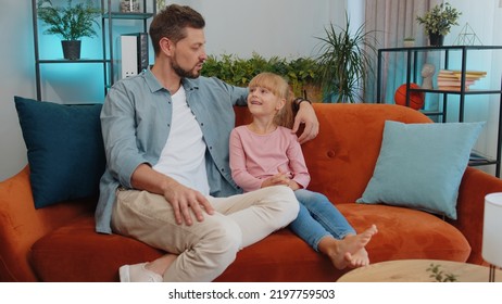 Young Loving Man Dad Talking To Little 7s Daughter Toddler Together On Couch At Home. School Kid And Father Having Warm Trustworthy Conversation, Good Relation. Understanding, Family Bond Concept