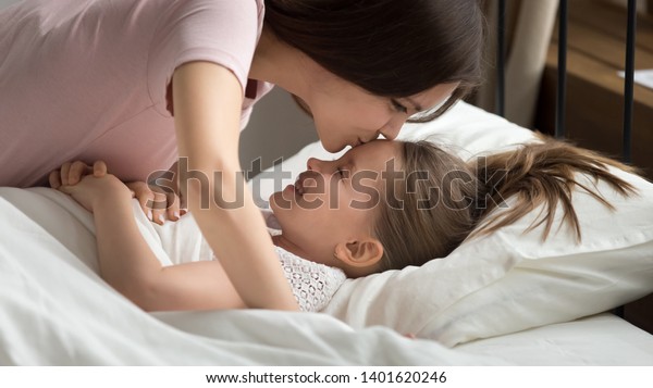 おでこに笑う若い愛情のある母親のキスは 甘い夢とおやすみを望み 思いやりのある母親は 小さな未就学児の子どもをベッドに入れ 昼の昼寝の前に抱きしめる の写真素材 今すぐ編集