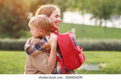 Young Loving Mother Hugging Embracing Little Son Schoolboy With Red Backpack And Saying Goodbye Before First Day In School While Standing Together In Park , Loving Mom Leading Child To First Grade