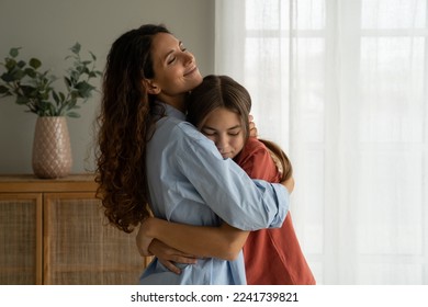 Young loving mother hugging her teenage daughter, mom demonstrating unconditional love for child, mommy cuddling supporting upset teen girl while spending time together at home. Mother-daughter bond 