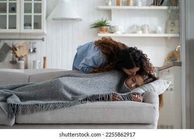 Young loving mother kissing daughter sleeping peacefully on couch during day nap time. Careful mommy giving kiss cute sleepy kid lying resting on sofa. Mom unconditional love, warmth and affection - Powered by Shutterstock