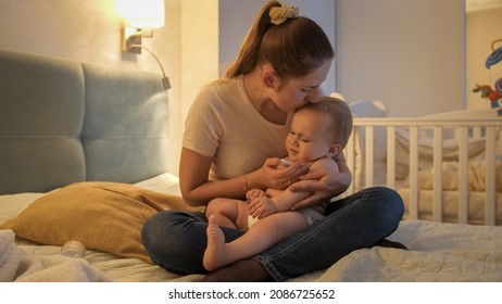 Young loving mother kissing her baby son while measuring his temperature with thermometer. - Shutterstock ID 2086725652