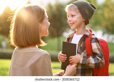 Young loving smiling mother leading son schoolboy with backpack to first grade, mom sitting down next to her little child and saying good bye before school while standing together outdoor on sunny day - Shutterstock ID 2030365712