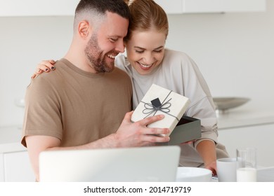 Young loving wife making surprise for husband for anniversary or birthday, congratulating him and giving present while having healthy breakfast in morning at kitchen, happy man opening gift box - Shutterstock ID 2014719719
