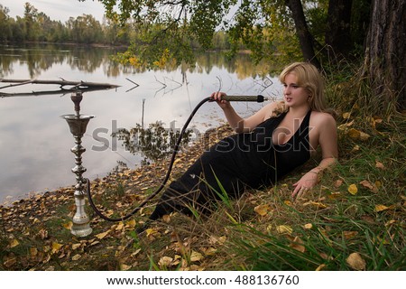 Young lush blonde smokes a hookah in the nature in the forest