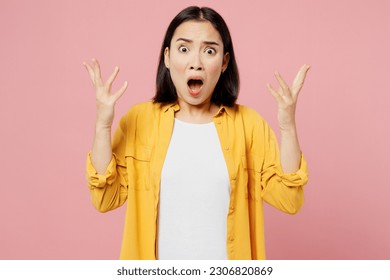 Young mad sad angry shocked woman of Asian ethnicity wear yellow shirt white t-shirt look camera scream spread hands isolated on plain pastel light pink background studio portrait. Lifestyle concept