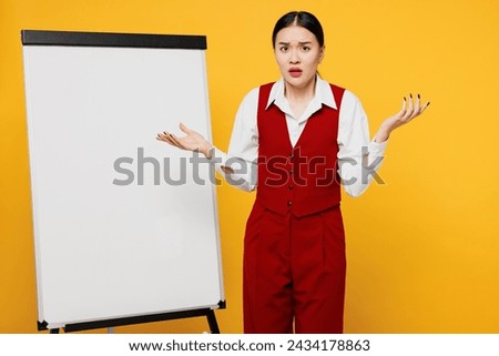 Young mad sad lawyer employee business woman of Asian ethnicity wear formal red vest shirt work at office stand near blank white board spread hands isolated on plain yellow background. Career concept