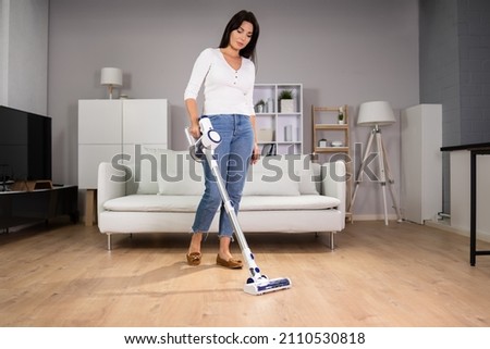 Young Maid Cleaning Floor With Handheld Vacuum Cleaner