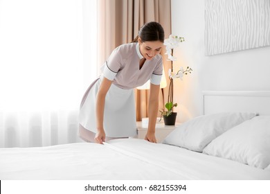 Young maid making bed in light hotel room - Shutterstock ID 682155394