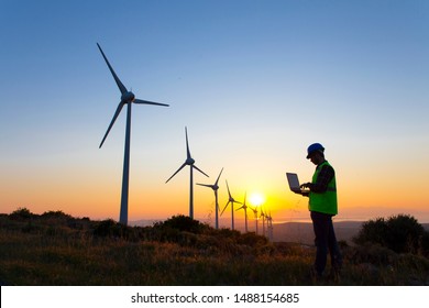Young maintenance engineer man working in wind turbine farm at sunset