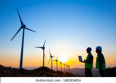 Young Maintenance Engineer Team Working In Wind Turbine Farm At Sunset Stock Photo