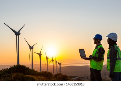 Young Maintenance Engineer Team Working In Wind Turbine Farm At Sunset