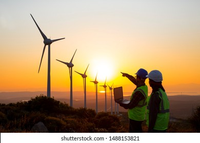 Young Maintenance Engineer Team Working In Wind Turbine Farm At Sunset