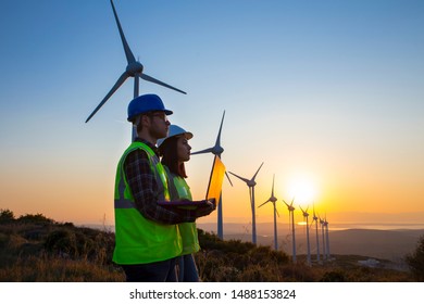 Young Maintenance Engineer Team Working In Wind Turbine Farm At Sunset