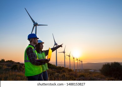Young maintenance engineer team working in wind turbine farm at sunset