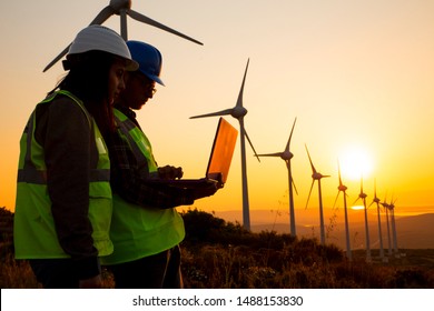 Young Maintenance Engineer Team Working In Wind Turbine Farm At Sunset