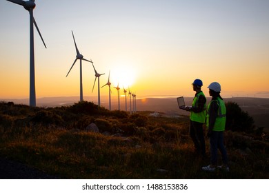 Young Maintenance Engineer Team Working In Wind Turbine Farm At Sunset