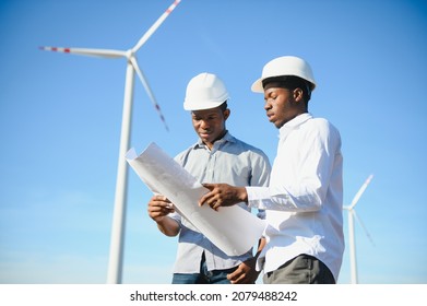 Young Maintenance Engineer Team Working In Wind Turbine Farm At Sunset Stock Photo